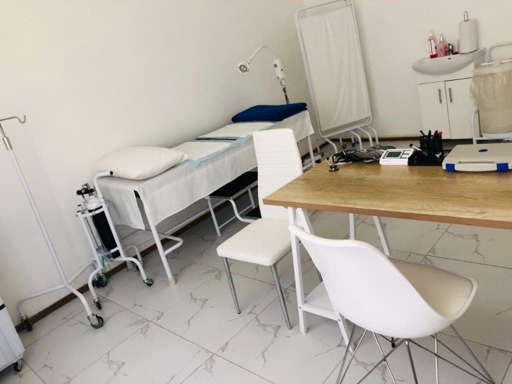 Examination room with desk, bed, and clinical equipment at Elshaddai Health Care Centre